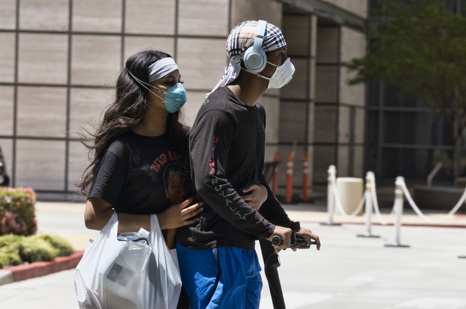 A couple wearing protective masks from the coronavirus ride a scooter down the street past the Ronald Reagan UCLA Medical Center in the Westwood section of Los Angeles, California, U.S. on May 15, 2020. (AP Photo)