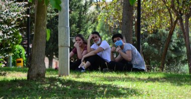 Three teenagers wearing masks sit in a park during the relaxation of the curfew for people under 20, in Adana, Turkey, May 15, 2020. (DHA Photo) 