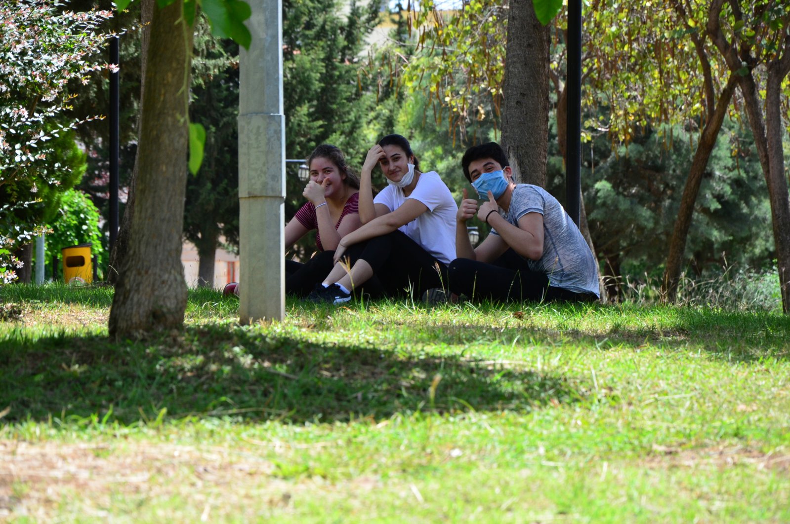 Three teenagers wearing masks sit in a park during the relaxation of the curfew for people under 20, in Adana, Turkey, May 15, 2020. (DHA Photo) 