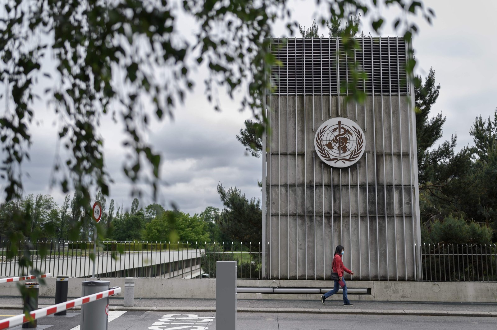 A woman wearing a protective facemask walks underneath a sign of the World Health Organization (WHO) in Geneva next to their headquarters, May 12, 2020. (AFP Photo)