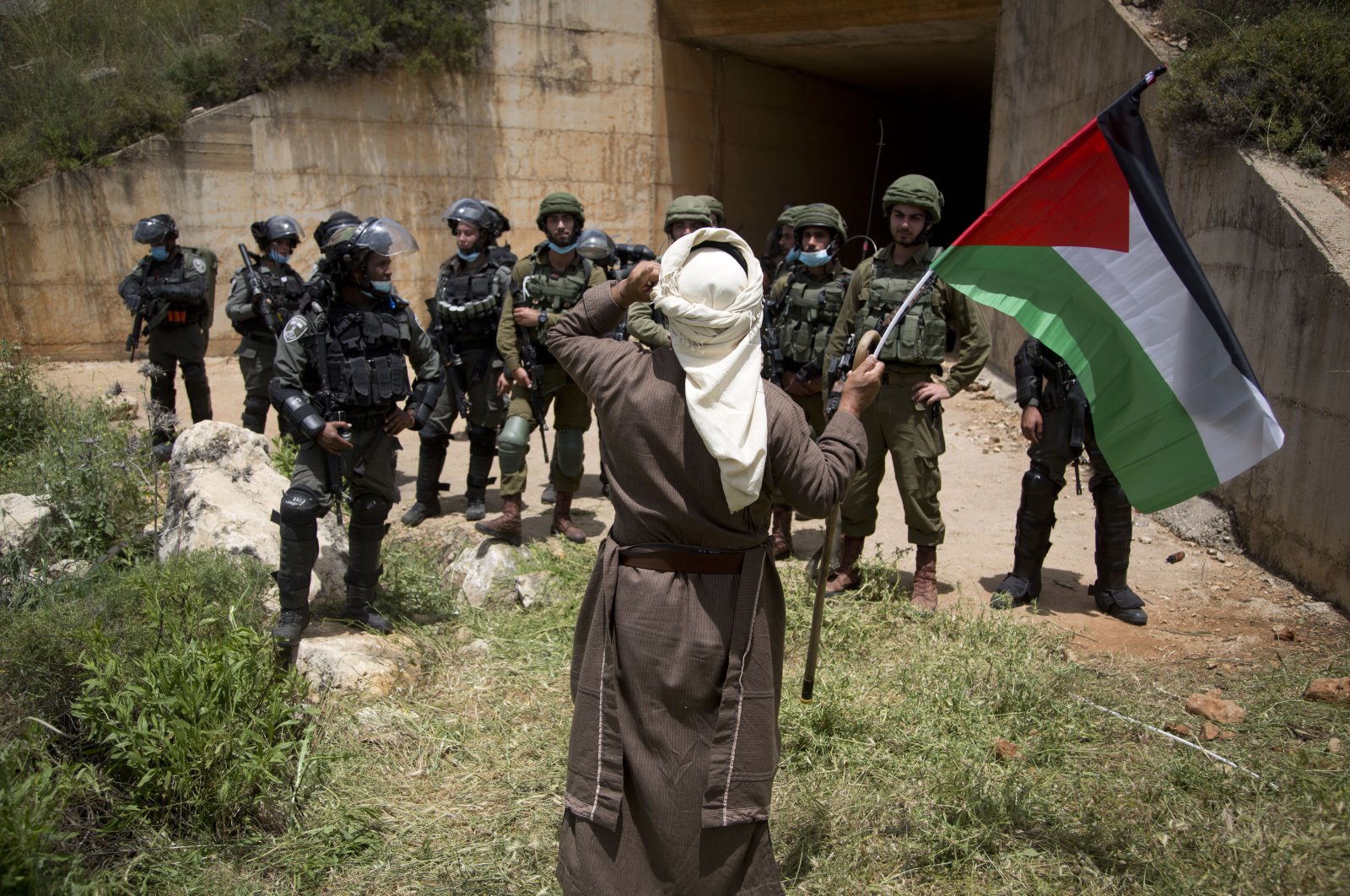 A Palestinian holds the national flag in front of Israeli border police during a protest marking the 72nd anniversary "Nakba," or catastrophe – a leading symbol against the Israeli annexations and occupations, near the West Bank city of Nablus, May 15, 2020. (AP Photo)