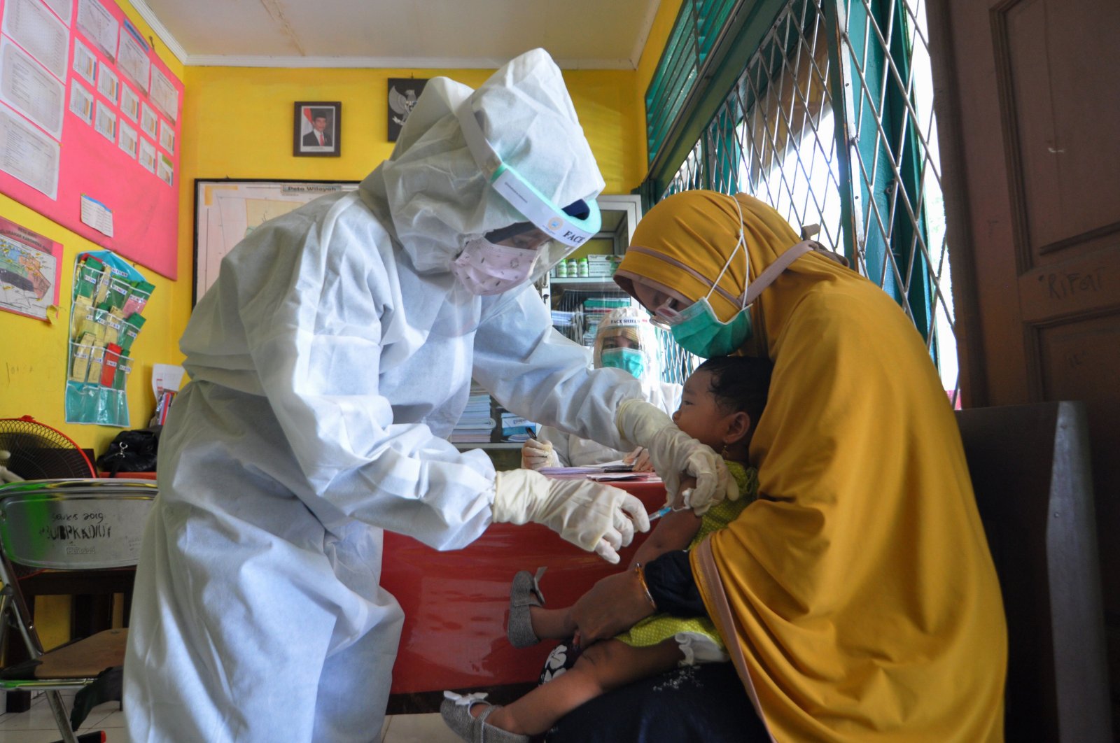 Nurses wearing protective gear give an injection of a vaccine for measles to a child at a health center in Palu, May 12, 2020. (AFP Photo)