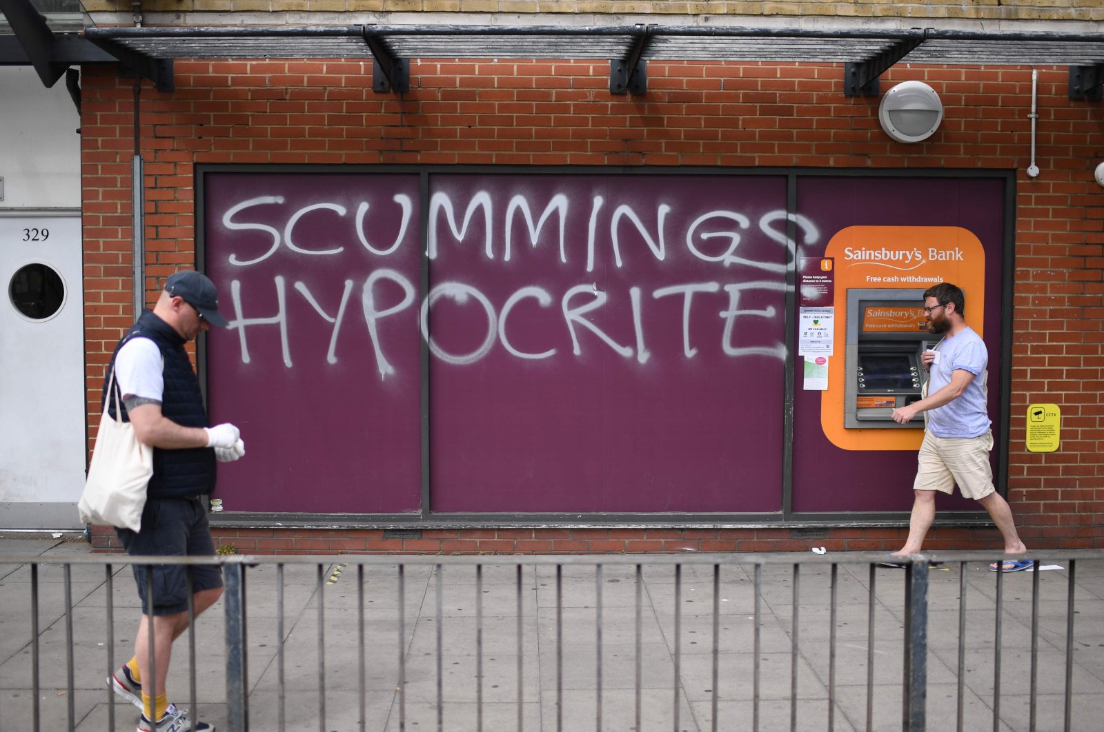 People walk past graffiti deriding number 10 special advisor Dominic Cummings outside a supermarket near his residence in north London on May 26, 2020 (AFP Photo)