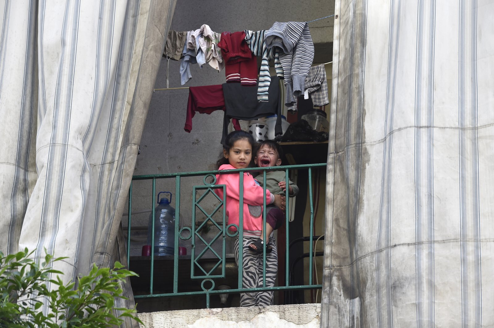 A Syrian refugee girl holds her crying younger brother as she looks on from a balcony in a residential building where Syrian refugees who have tested positive for the novel coronavirus remain quarantined in Beirut, Lebanon, May 20, 2020. (EPA Photo)