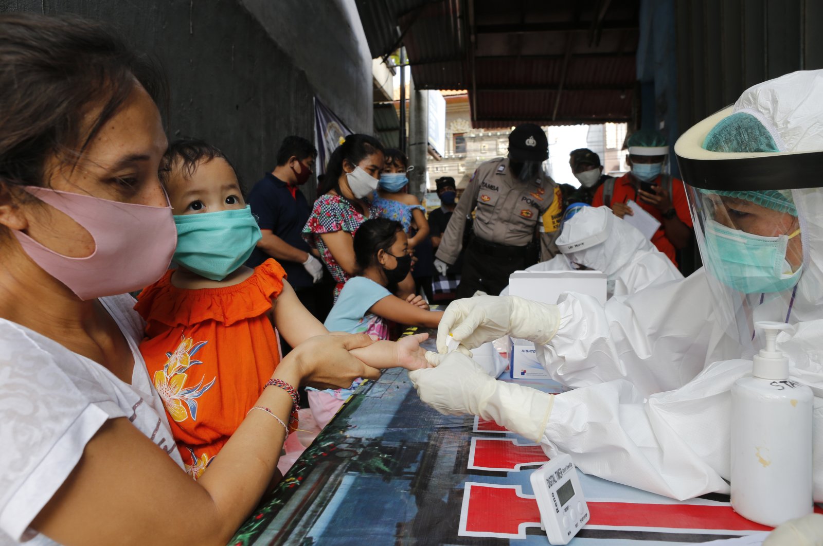 A mother holds her daughter to receive a coronavirus antibody test from health workers at a village in Bali, Indonesia, May 27, 2020. (AP Photo)