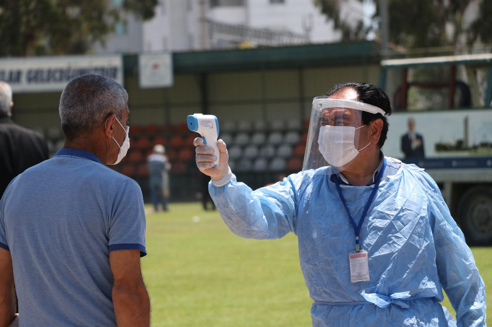 An official measures temperature of a citizen before Friday prayer in a stadium, Mersin, on May 29, 2020. (IHA Photo)