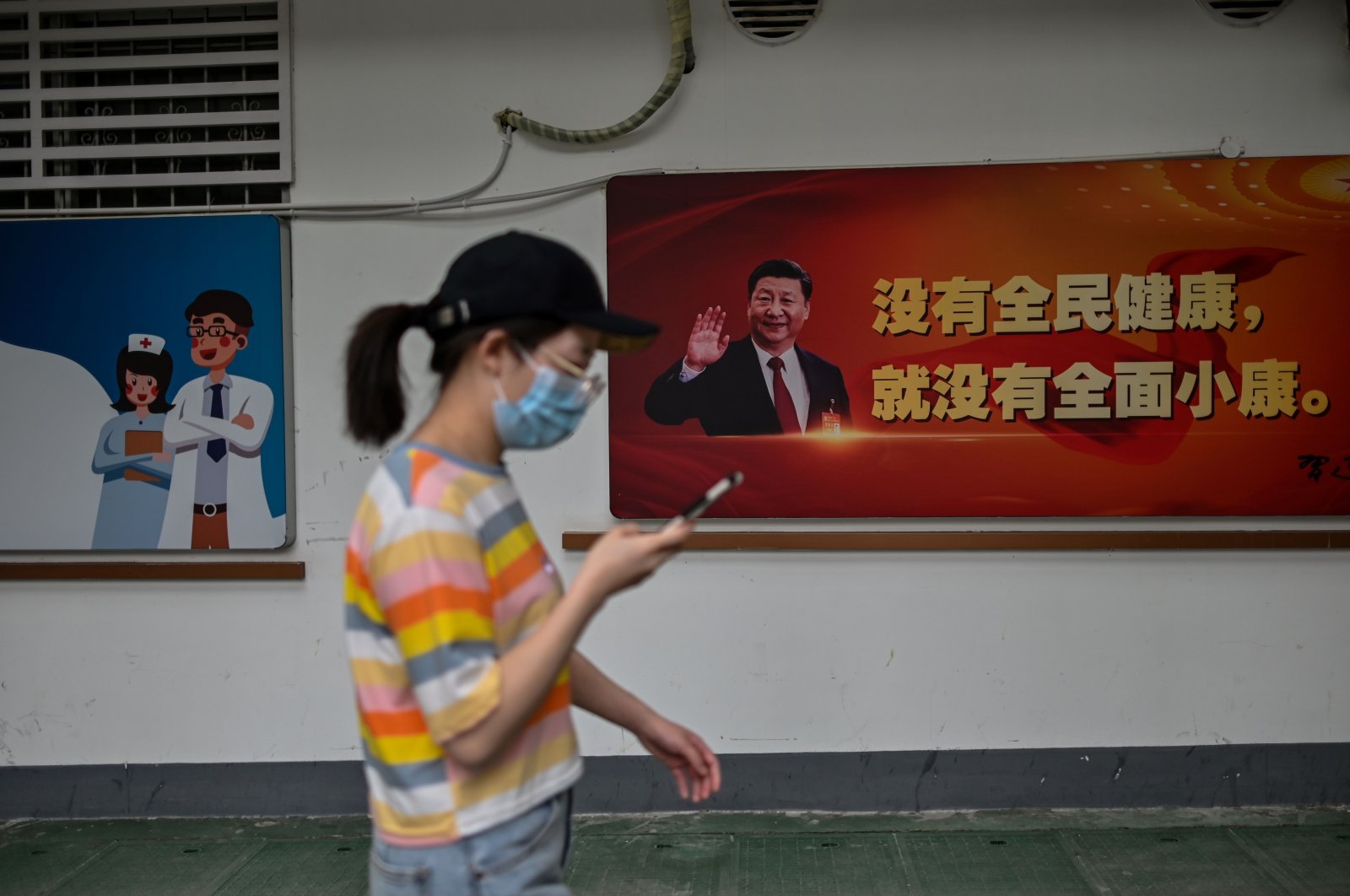 A woman walks past a photograph of China's President Xi Jinping displayed outside a hospital, Wuhan, May 28, 2020. (AFP Photo)