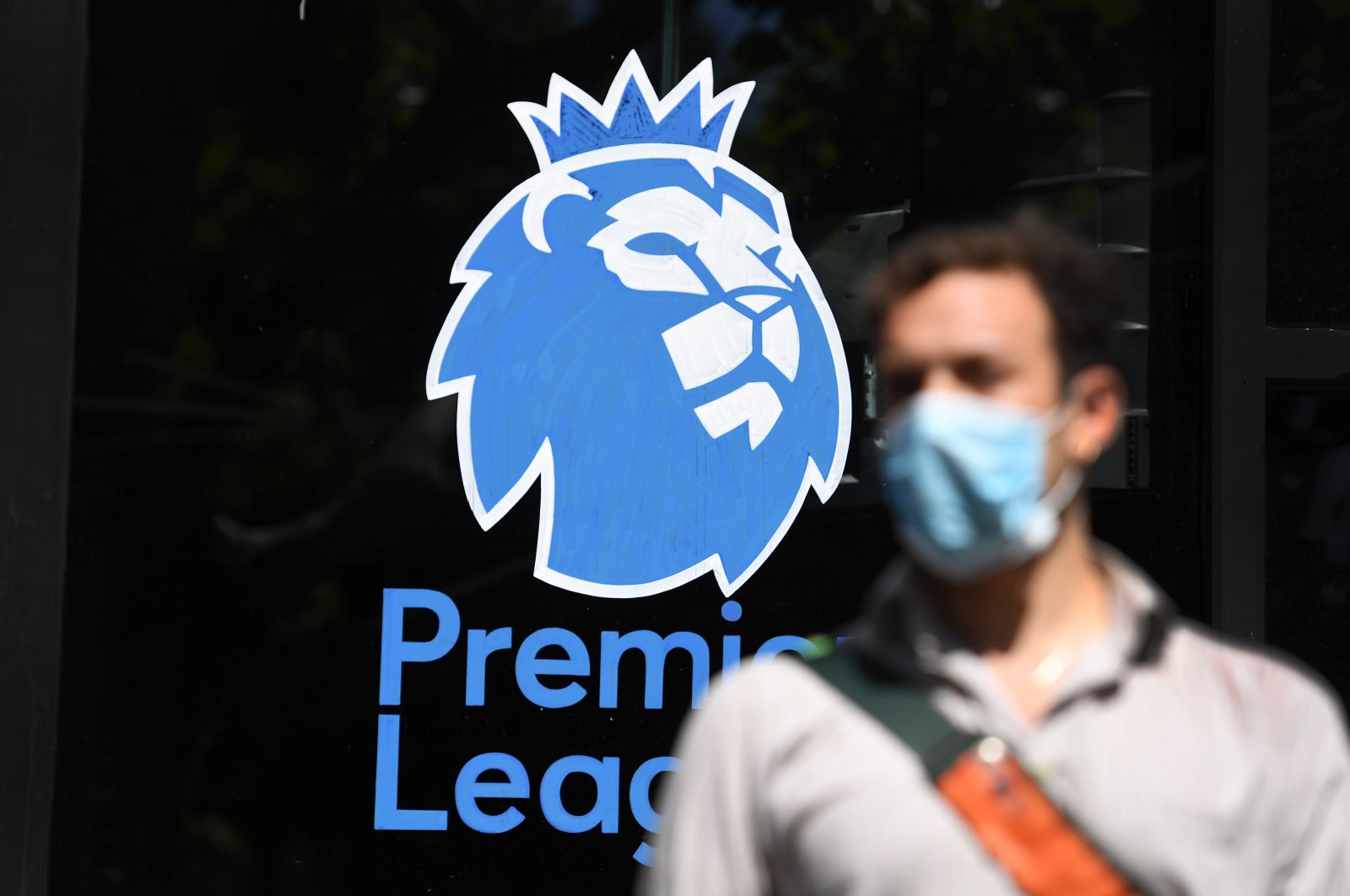 A man wearing a protective mask walks past the English Premier League logo in London, May 29, 2020. (EPA Photo)