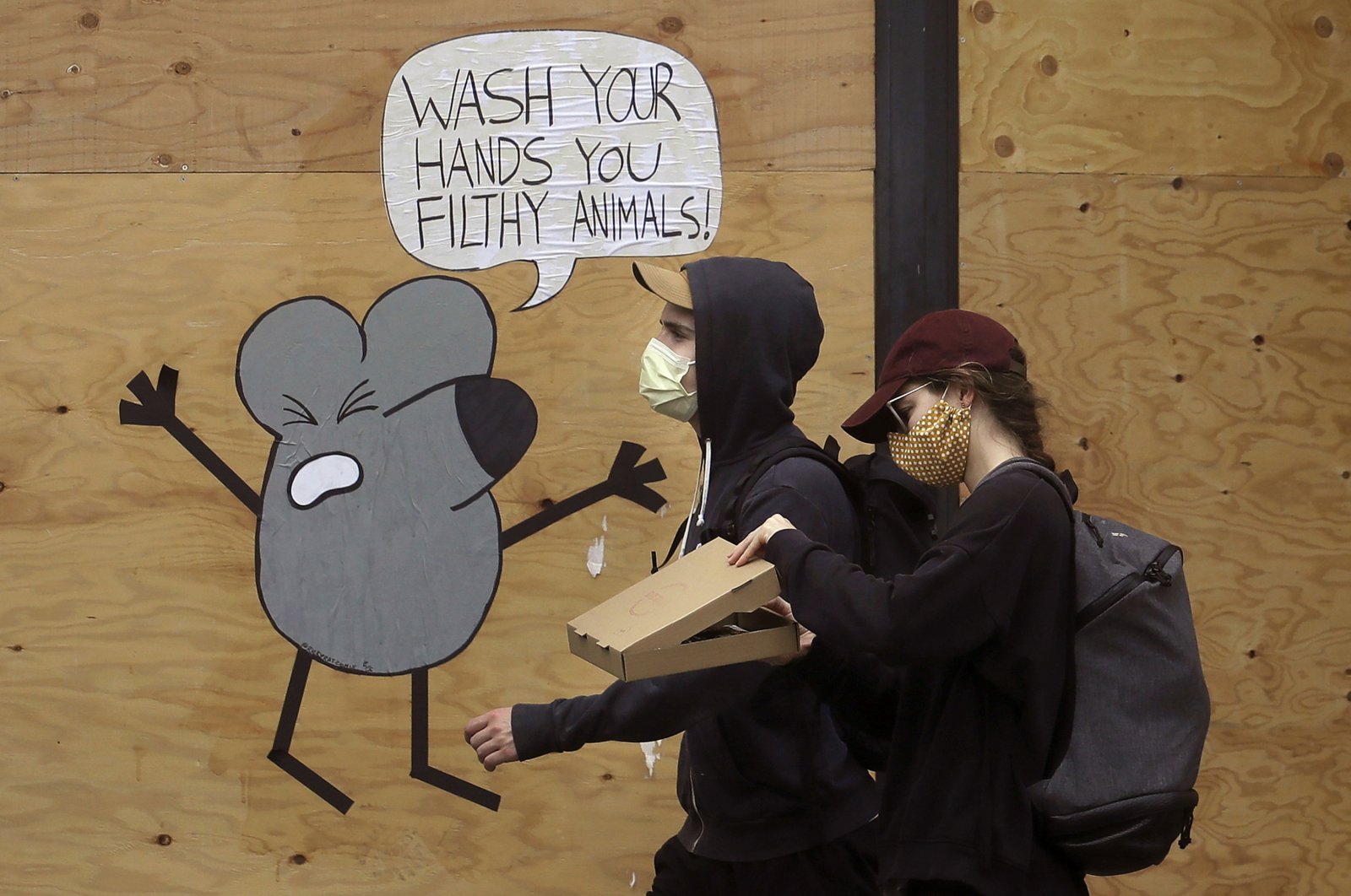 A man and woman wearing masks to prevent the spread of the coronavirus walk past a cartoon advising people to wash their hands on a boarded-up storefront in San Francisco, California, U.S., May 2, 2020. (AP Photo)