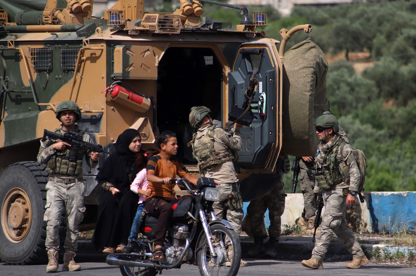 A youth rides a motorcycle carrying a woman and children past a Turkish armoured vehicle part of a joint Turkish-Russian military patrol along the M4 highway in Ariha in the opposition-held northwestern Syrian province of Idlib, June 2, 2020. (AFP Photo)