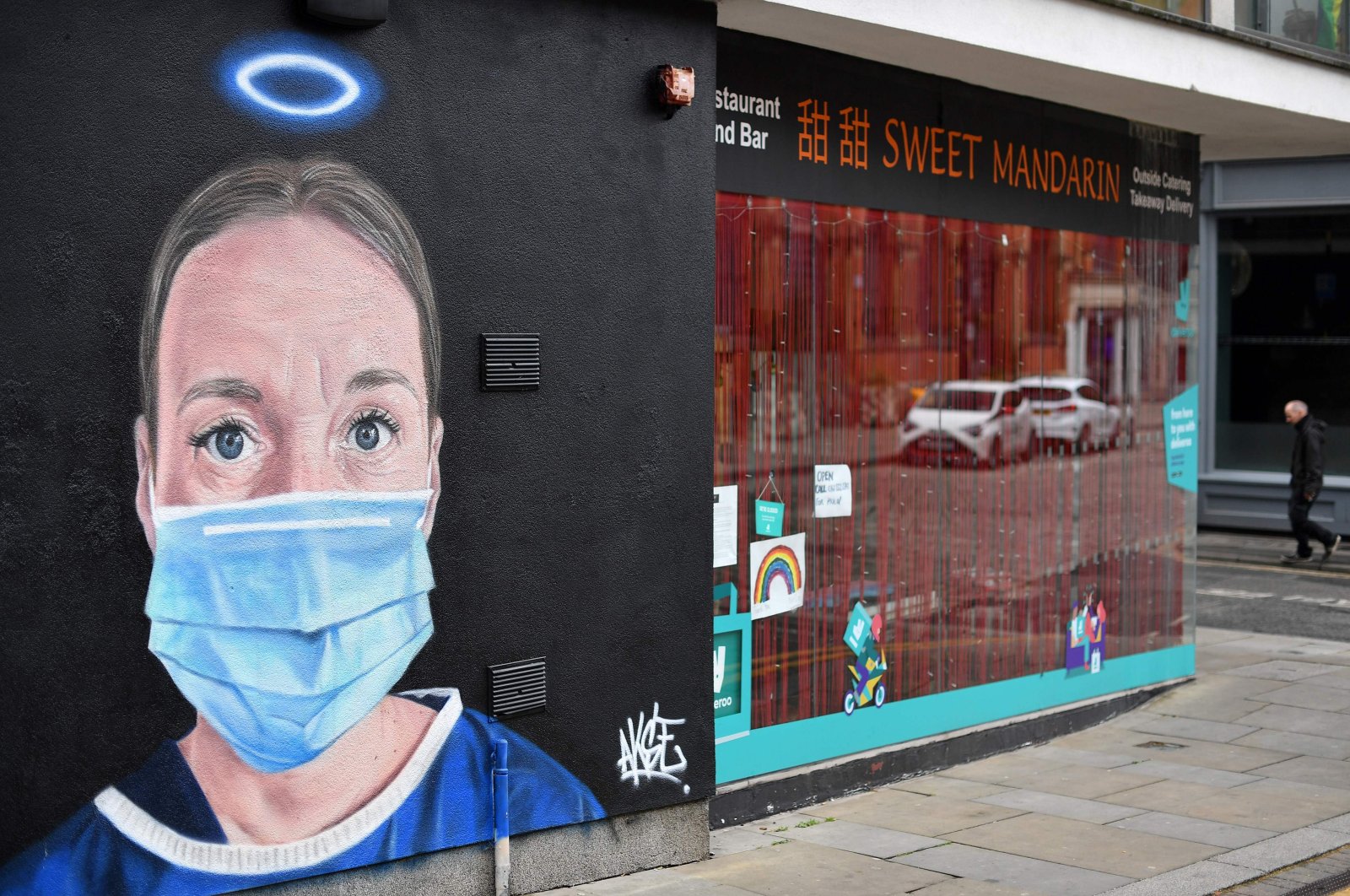 A pedestrian walks past street art graffiti, depicting a nurse with an angel's halo above her head, Manchester, June 3, 2020. (AFP Photo)