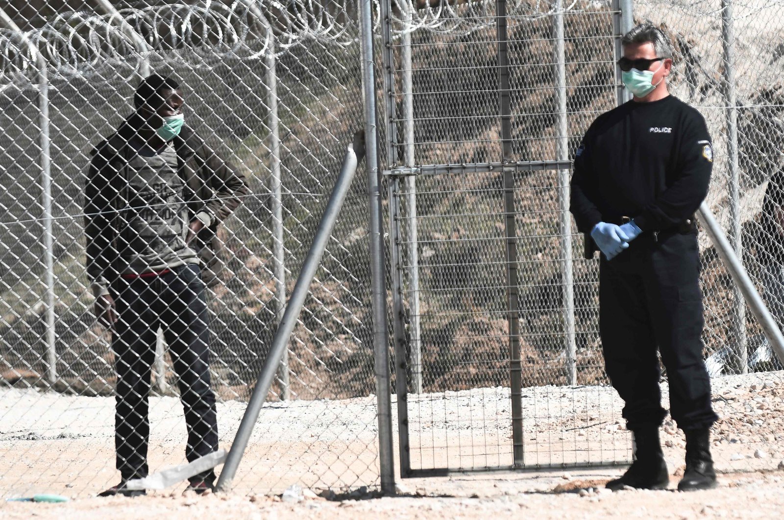 A migrant looks at a Greek police officer at a closed camp at Kleidi near Promahonas, northern Greece, March 21, 2020. (AFP Photo)