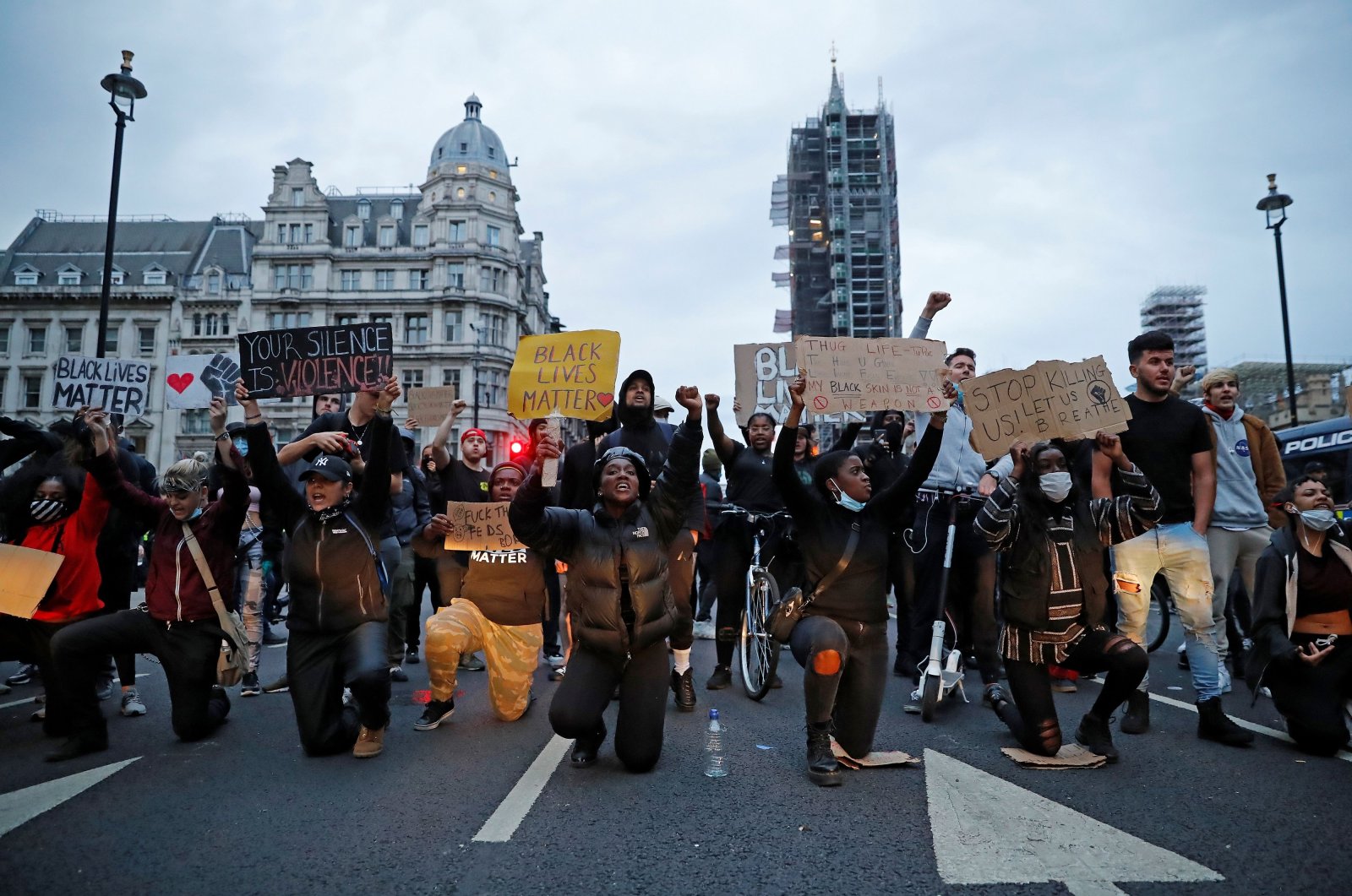Protestors hold placards as they kneel in front of police vans in Parliament Square, during an anti-racism demonstration in London, on June 3, 2020. (AFP Photo)