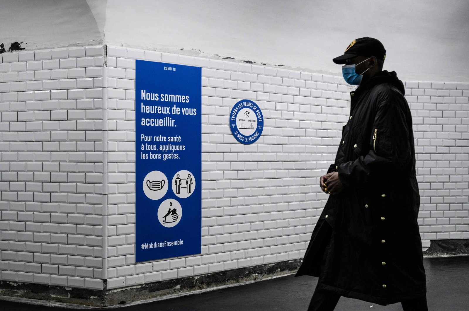 A commuter wearing a protective face mask walks past safety guideline signs in a metro station in Paris, France, May 14, 2020. (AFP Photo)