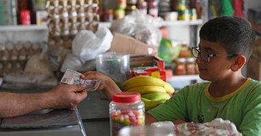 A boy pays a merchant with a Turkish lira banknote at a shop in the town of Jinderes, in the Afrin district of northwestern Syria, June 10, 2020. (AFP Photo)