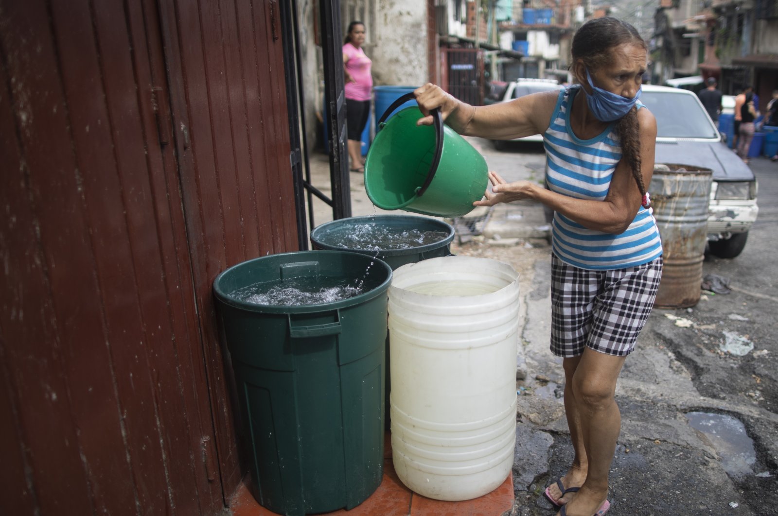 A woman, wearing a protective face mask as a measure to help curb the spread of the coronavirus, fills a big container with water provided by a government water truck, in the Petare slum of Caracas, June 10, 2020. (AP)