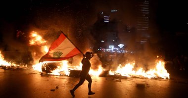 A protester holding the Lebanese flag runs as protesters block the Jounieh Tripoli highway with flaming tires, Beirut, Lebanon, June 11, 2020. (AFP Photo)