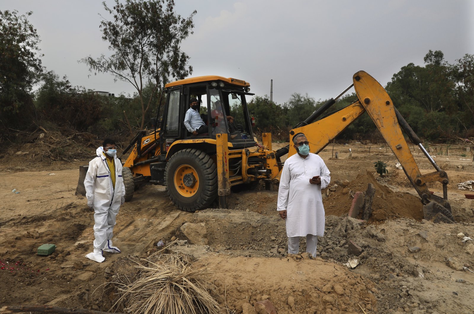 People wait for others to join as an earthmover digs a grave for the burial of a COVID-19 victim at a cemetery in New Delhi, India, June 5, 2020. (AP Photo)