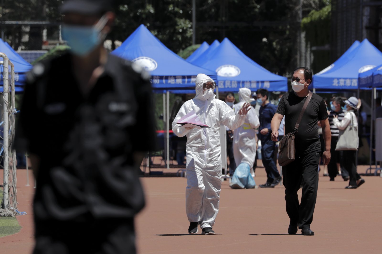 A worker in protective suit chats with a resident who was either living surrounding the Xinfadi wholesale market or have visited to the market to get a nucleic acid test at a stadium in Beijing, Sunday, June 14, 2020. (AP Photo)