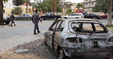 Libyan policemen walk near a damaged car during a security deployment in Tarhouna city, June 11, 2020. (REUTERS)