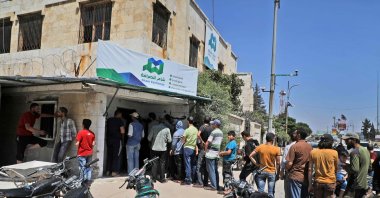Syrians queue outside a currency exchange shop in Syria's northwestern city of Idlib, June 15, 2020. (AFP Photo)