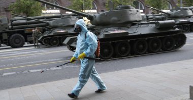 A municipal employee in a protective suit disinfects an area as a measure against the coronavirus outbreak while World War II Soviet-made tanks wait to start a rehearsal for the Victory Day military parade in Moscow, Russia, June 17, 2020. (AP Photo)