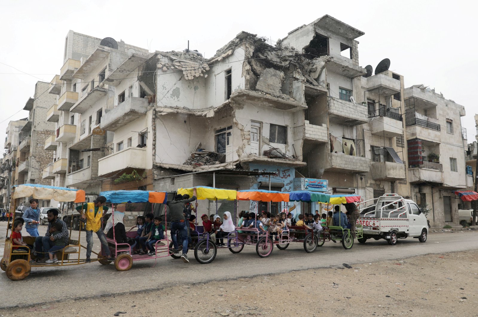 Children ride in carts past a damaged building on the first day of the Muslim holiday of Eid al-Fitr amid the global outbreak of the coronavirus, in the opposition-held Idlib city, northwest Syria, May 24, 2020. (REUTERS Photo)