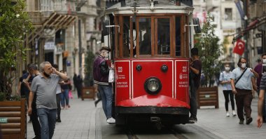 People, wearing protective masks against the spread of coronavirus, walk and use the tram on Istiklal street, the main shopping street in Istanbul, June 18, 2020. (AP Photo)