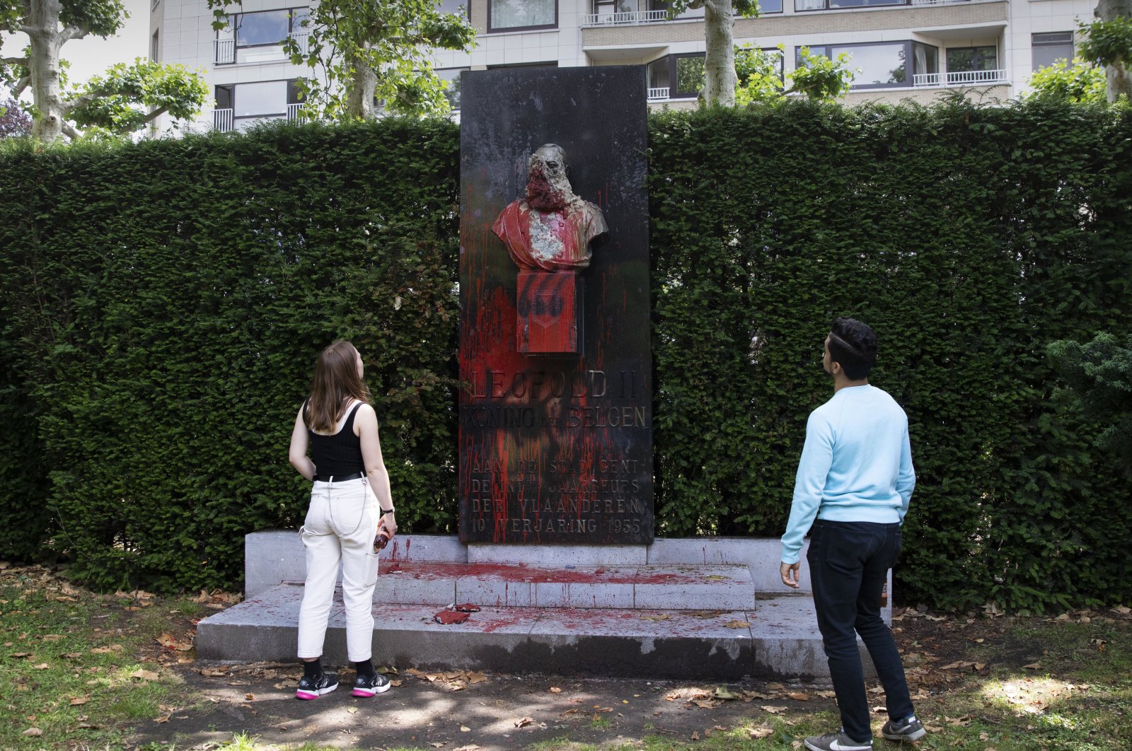 A couple stop to look at a bust of Belgium's King Leopold II, which has been damaged by red paint, graffiti and cement, at a park in Ghent, Belgium on Friday, June 19, 2020. Protests sweeping the world after George Floyd's death in the U.S. have added fuel to a movement to confront Europe's role in the slave trade and its colonial past.(AP Photo)