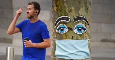 A man walks past a tree with a face mask and eyes stapled to it in Melbourne, Australia, April 26, 2020. (AAP Image via Reuters)