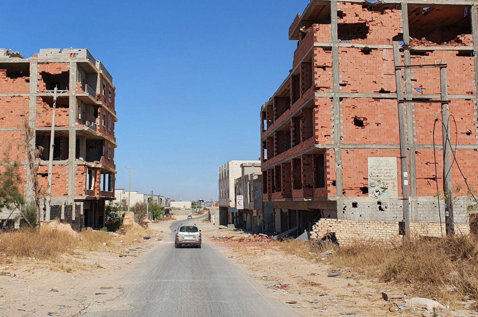 A car advances on an empty road between damaged buidlings in the Salaheddin district south of the Libyan capital Tripoli, June 21, 2020. (AFP)