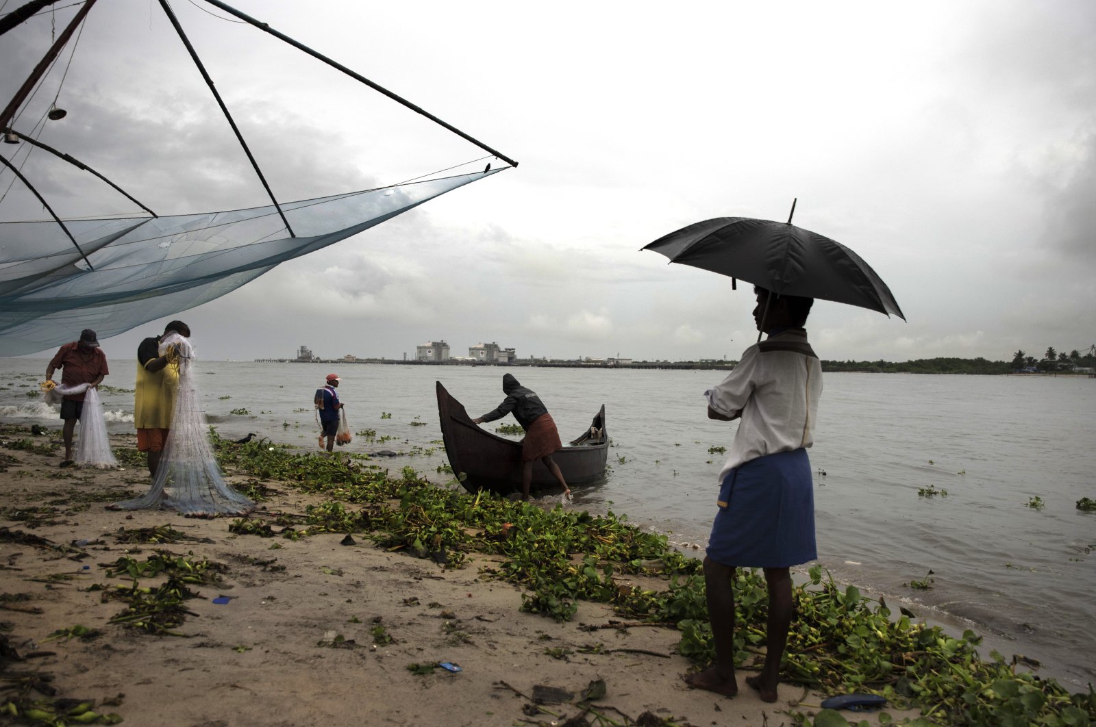 A man holding an umbrella watches fishermen at work on the Arabian sea coast during monsoon rains in Kochi, Kerala state, India, June 22 2020. (AP Photo)