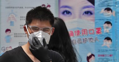 A man wearing gloves adjusts his protective face mask as he walks by posters showing a proper way to wear a face mask in Beijing, June 28, 2020. (AP Photo)