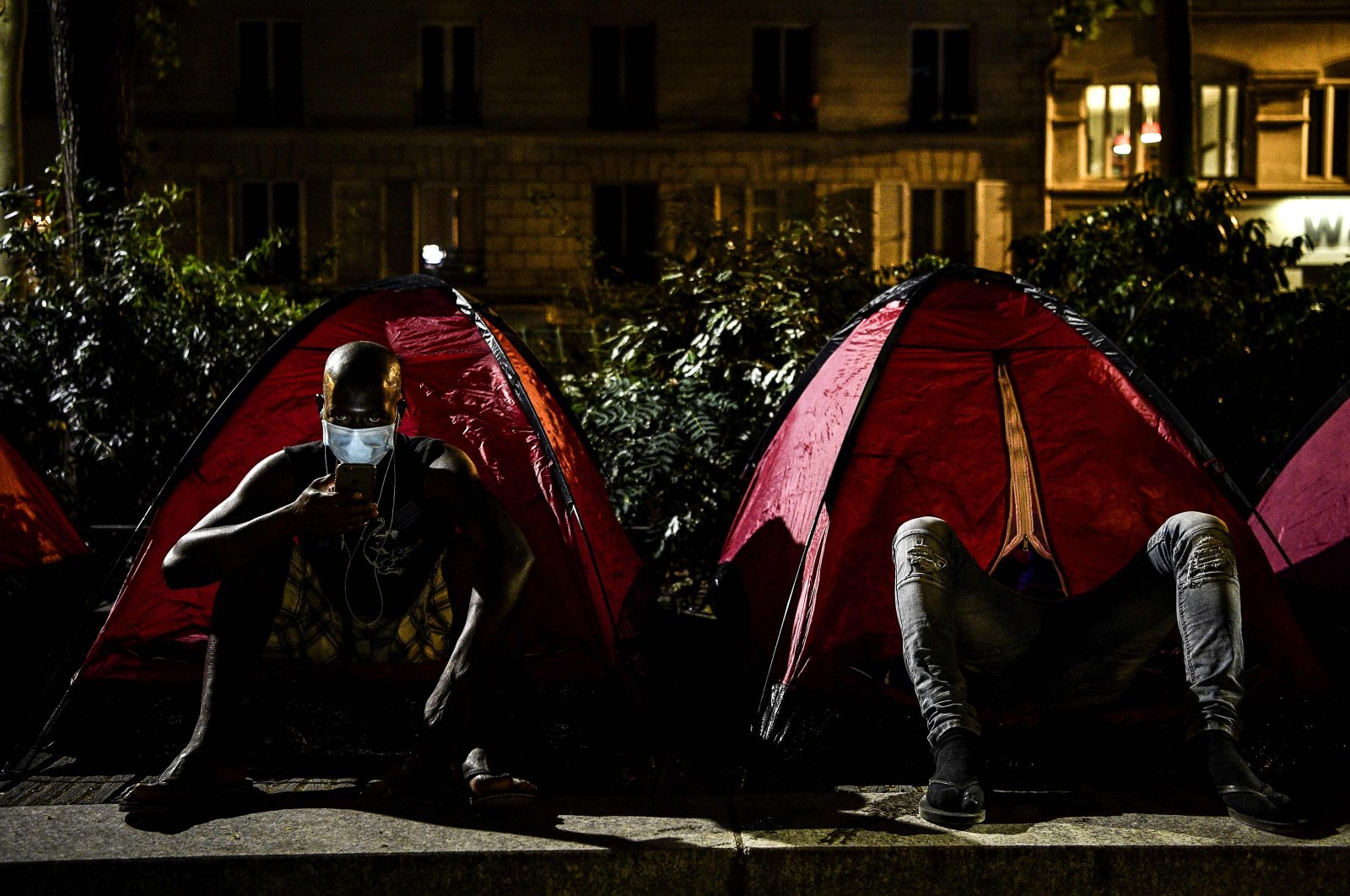 A young migrant checks his phone outside a tent at a makeshift camp set up by volunteers of charities Medecins Sans Frontieres (MSF – Doctors Without Borders) and Utopia 56 at a public park in Paris early on June 30, 2020. (AFP Photo)