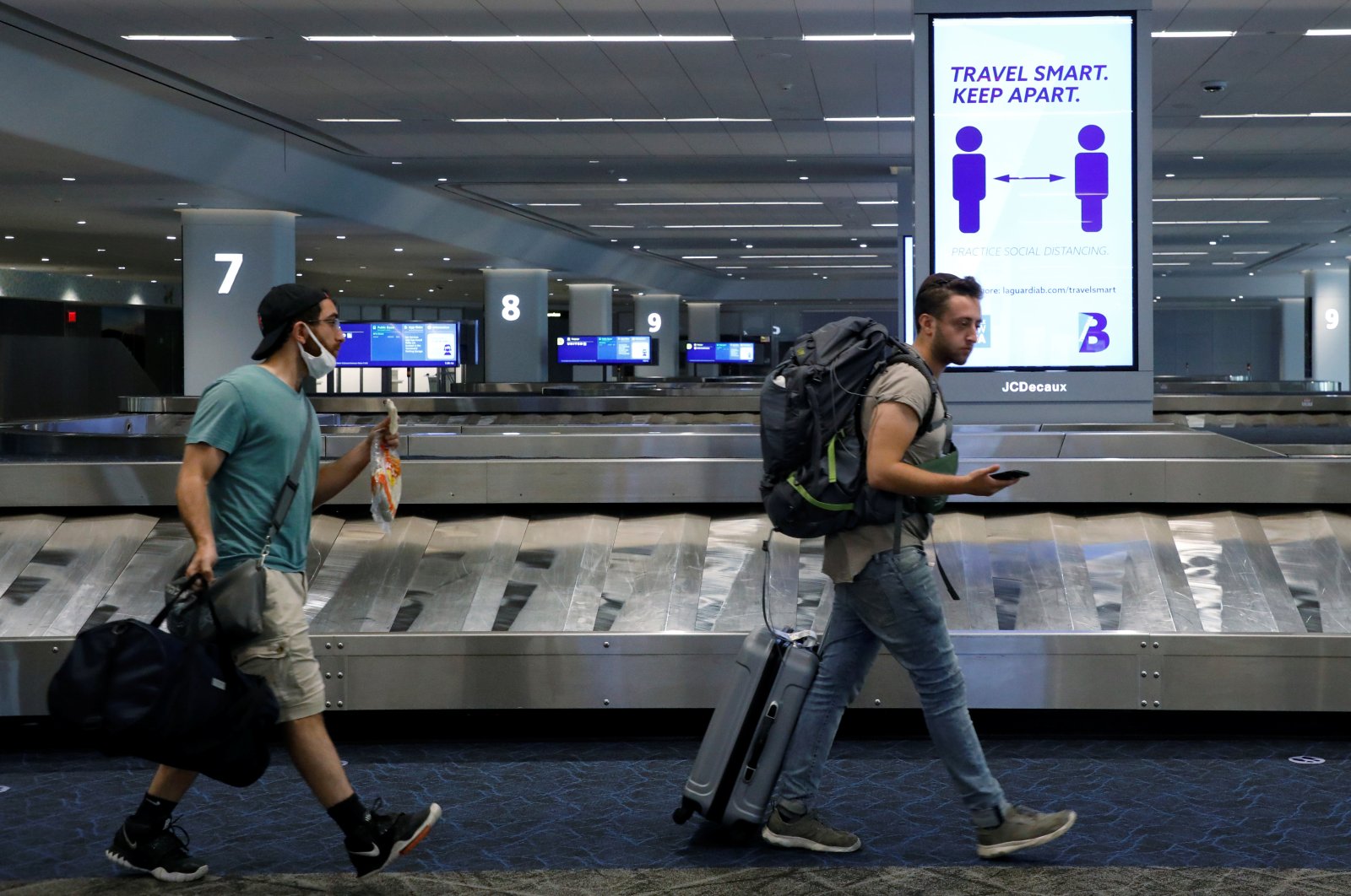 Travelers pass a sign alerting them to distance at LaGuardia Airport, during the outbreak of the coronavirus disease (COVID-19), in New York, U.S., June 29, 2020. (Reuters Photo)