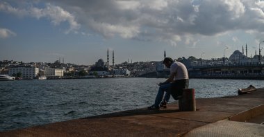A man sits near the shore of the Golden Horn strait Süleymaniye Mosque (R), as the New Mosque (L) is seen in the background, Istanbul, June 24, 2020. (AFP Photo)