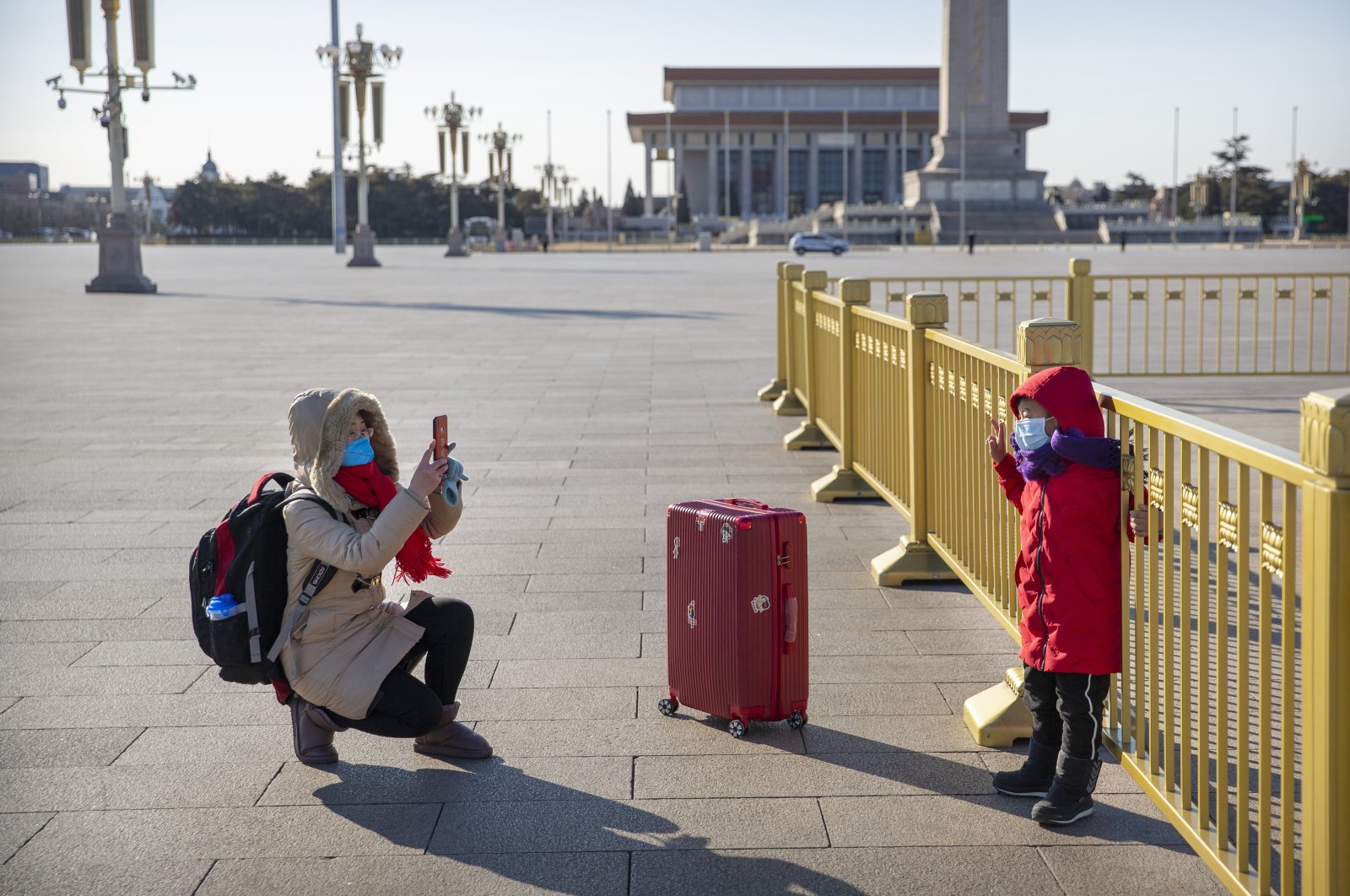 A woman wearing a face mask takes a photo of a child on a nearly empty Tiananmen Square in Beijing, Tuesday, Feb. 4, 2020. (AP Photo)