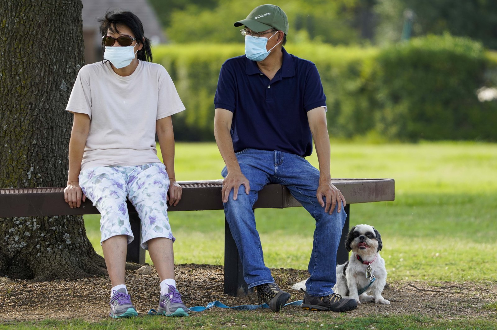 People wear face masks as they sit with their dog at Custer Park in Richardson, Texas, U.S., July 2, 2020. (The Dallas Morning News via AP)