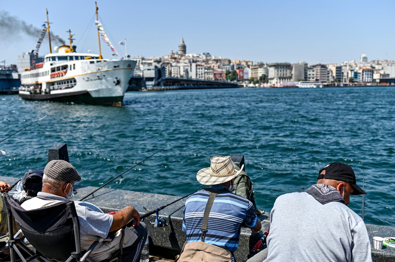 People wearing protective face masks to curb the spread of the novel coronavirus (COVID-19) fish on the Galata bridge, at Karakoy district in Istanbul on July 1, 2020. (AFP Photo)