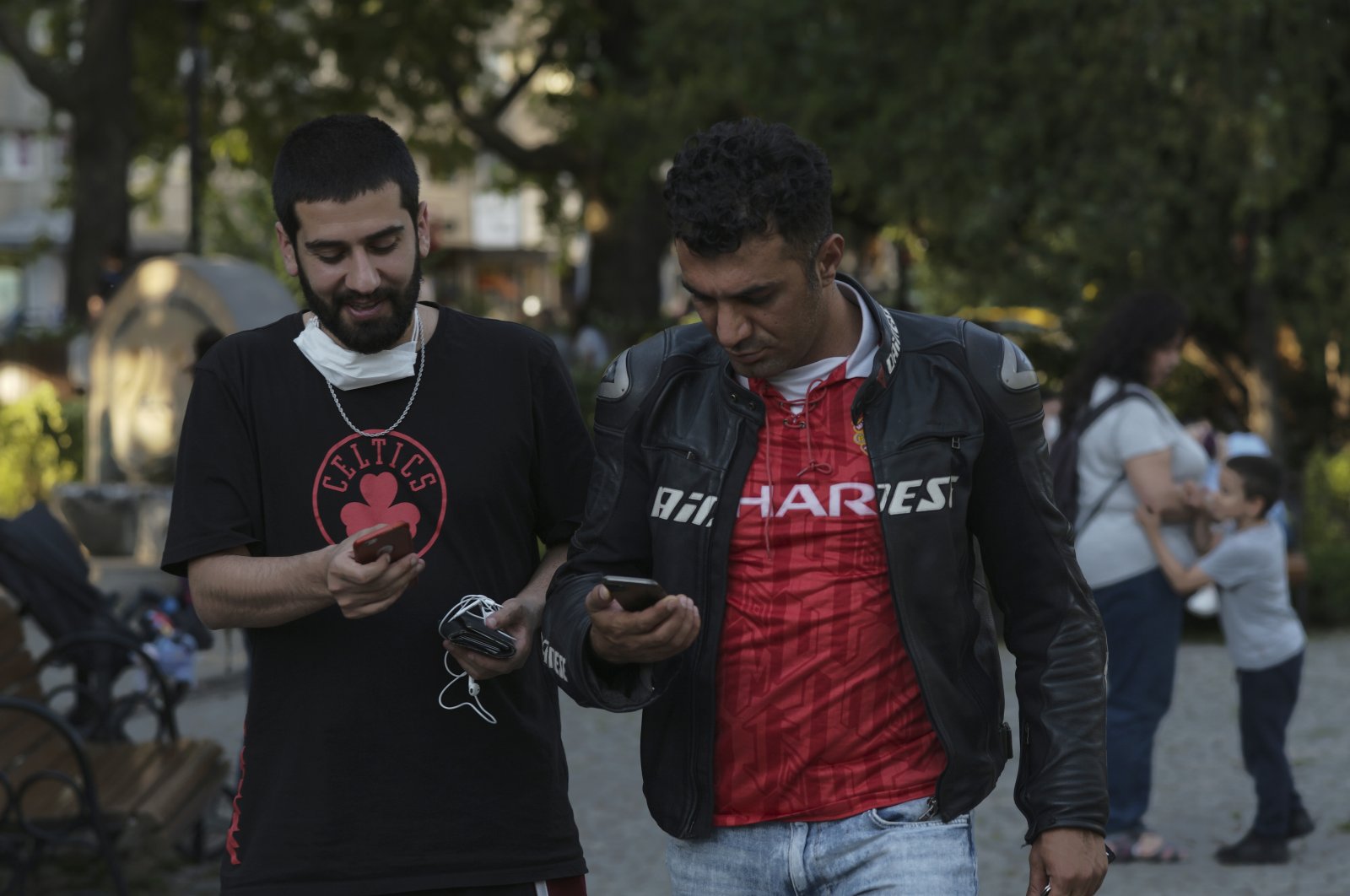 Two men without face coverings speak as they check their mobile phones in a public garden, in Ankara, Turkey, Tuesday, June 30, 2020. (AP Photo)