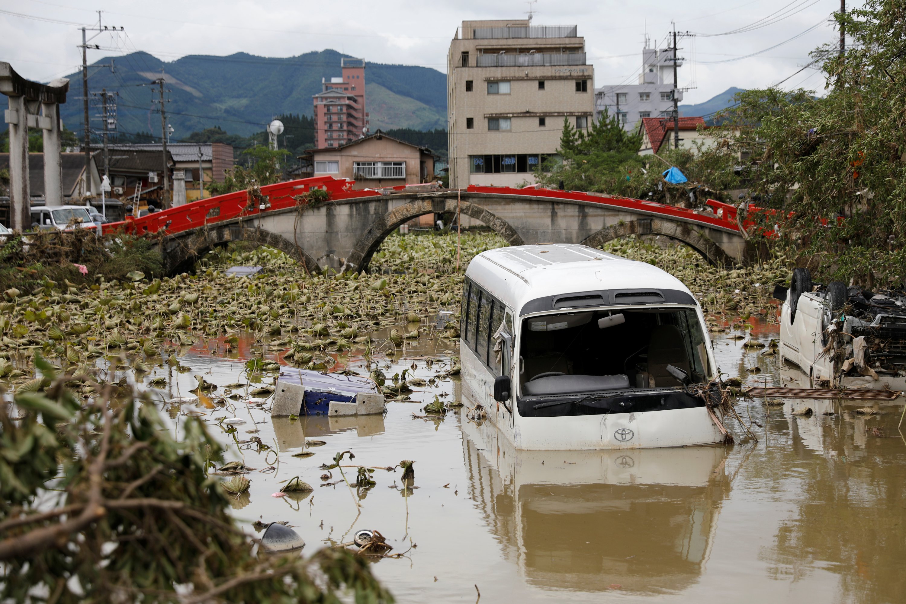 A broken bridge is seen in the back, as an overturned vehicle and a partially submerged bus are pictured in floodwaters caused by torrential rain in Hitoyoshi, Kumamoto Prefecture, southwestern Japan, July 8, 2020. (Reuters Photo)