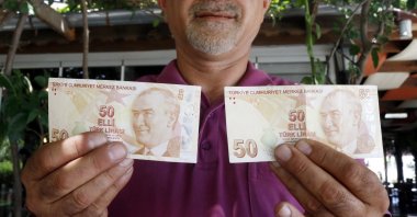 Mustafa Şahin holds up his misprinted TL 50 bill (L) and a normal one, Antalya, Turkey, July 9, 2020. (DHA Photo)