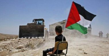 A Palestinian boy sits on a chair with a national flag as Israeli authorities demolish a school site in the village of Yatta in the occupied West Bank, July 11, 2018. (AFP Photo)