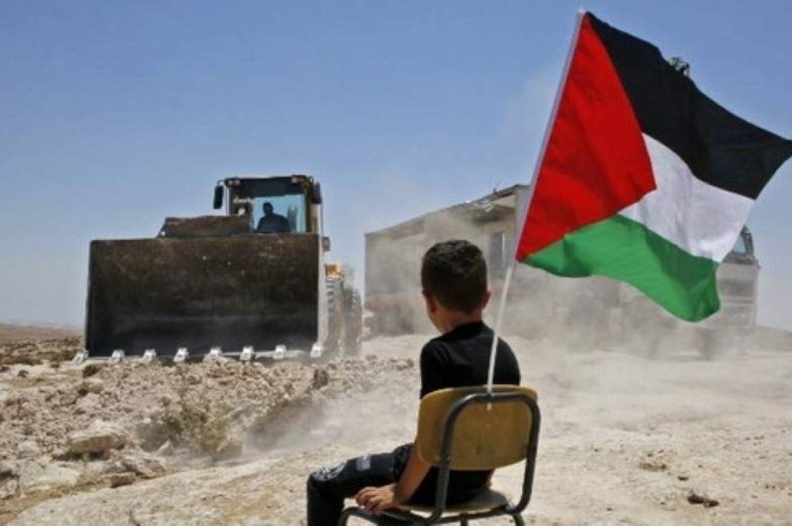 A Palestinian boy sits on a chair with a national flag as Israeli authorities demolish a school site in the village of Yatta in the occupied West Bank, July 11, 2018. (AFP Photo)