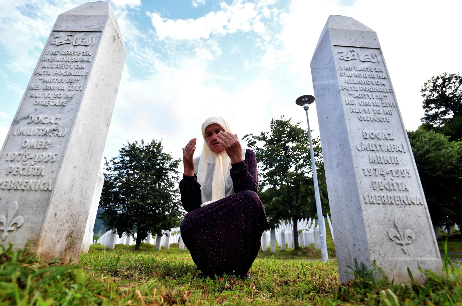 Bosnian Muslim woman Mejra Djogaz, 71, survivor of Srebrenica 1995 massacre, prays between her sons' tombstones, Omer, 19, and Munib, 21, her two sons killed in the massive killing of Srebrenica during Bosnia's 1992-95 war, at Potocari memorial center, near Srebrenica, July 3, 2020. (AFP)
