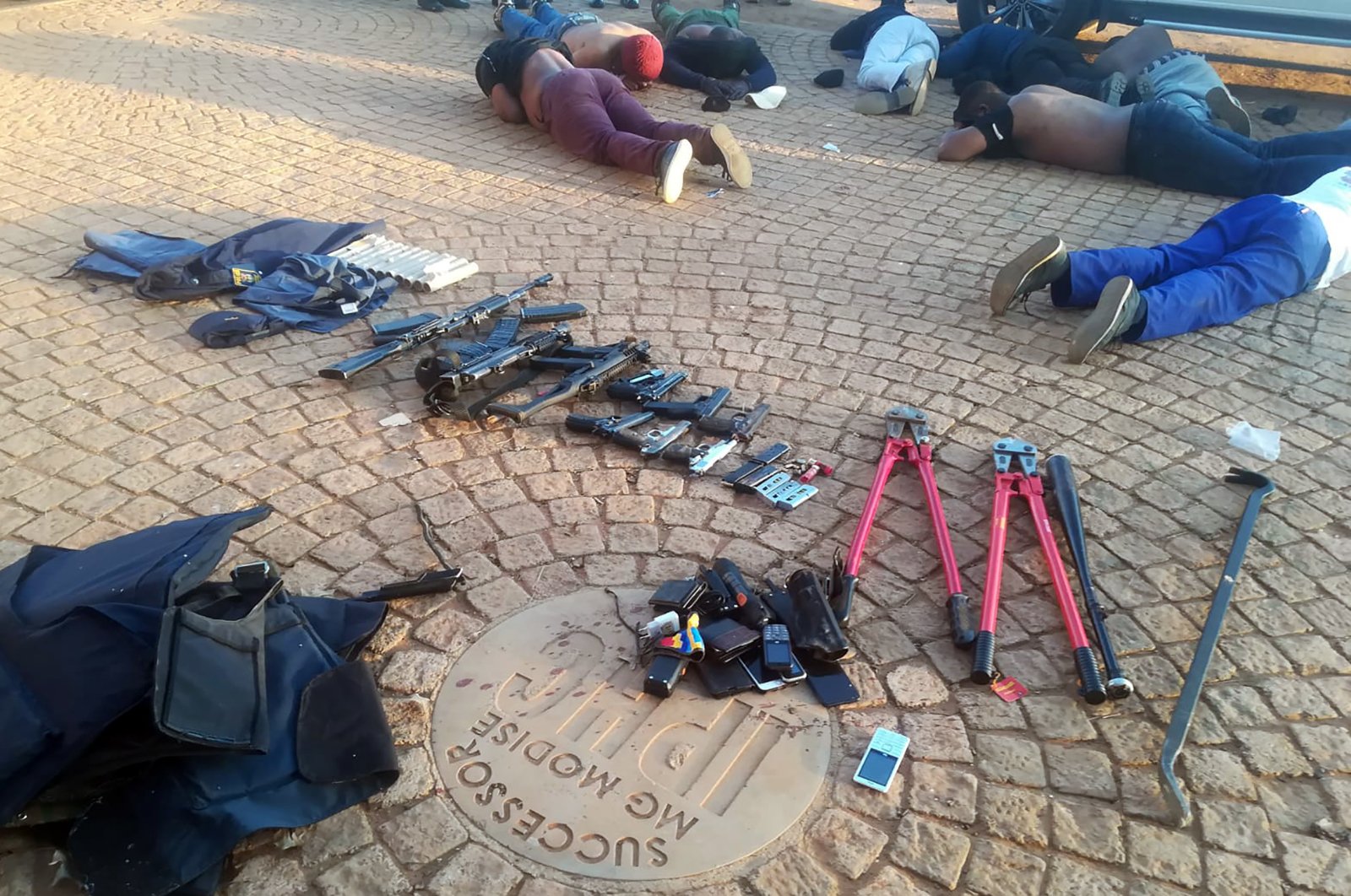 In this photo made available by the South African Police Services (SAPS), confiscated arms and ammunition, foreground, and arrested suspects, background, lay face-down at a church in Zuurbekom, near Johannesburg, Saturday, July 11, 2020. (AP Photo)