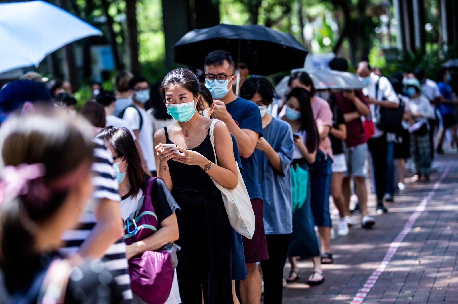 A woman (centre L) uses her phone while waiting to vote during primary elections in Hong Kong on July 12, 2020. (AFP Photo)