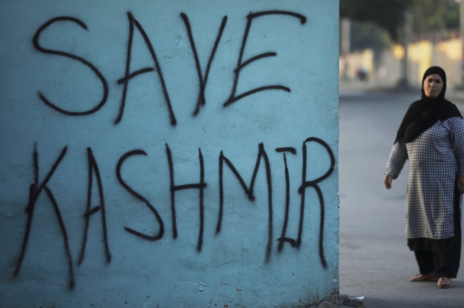 A Kashmiri woman stands next to a graffiti written on a wall during restrictions, Srinagar, Sept. 15, 2019. (REUTERS Photo)