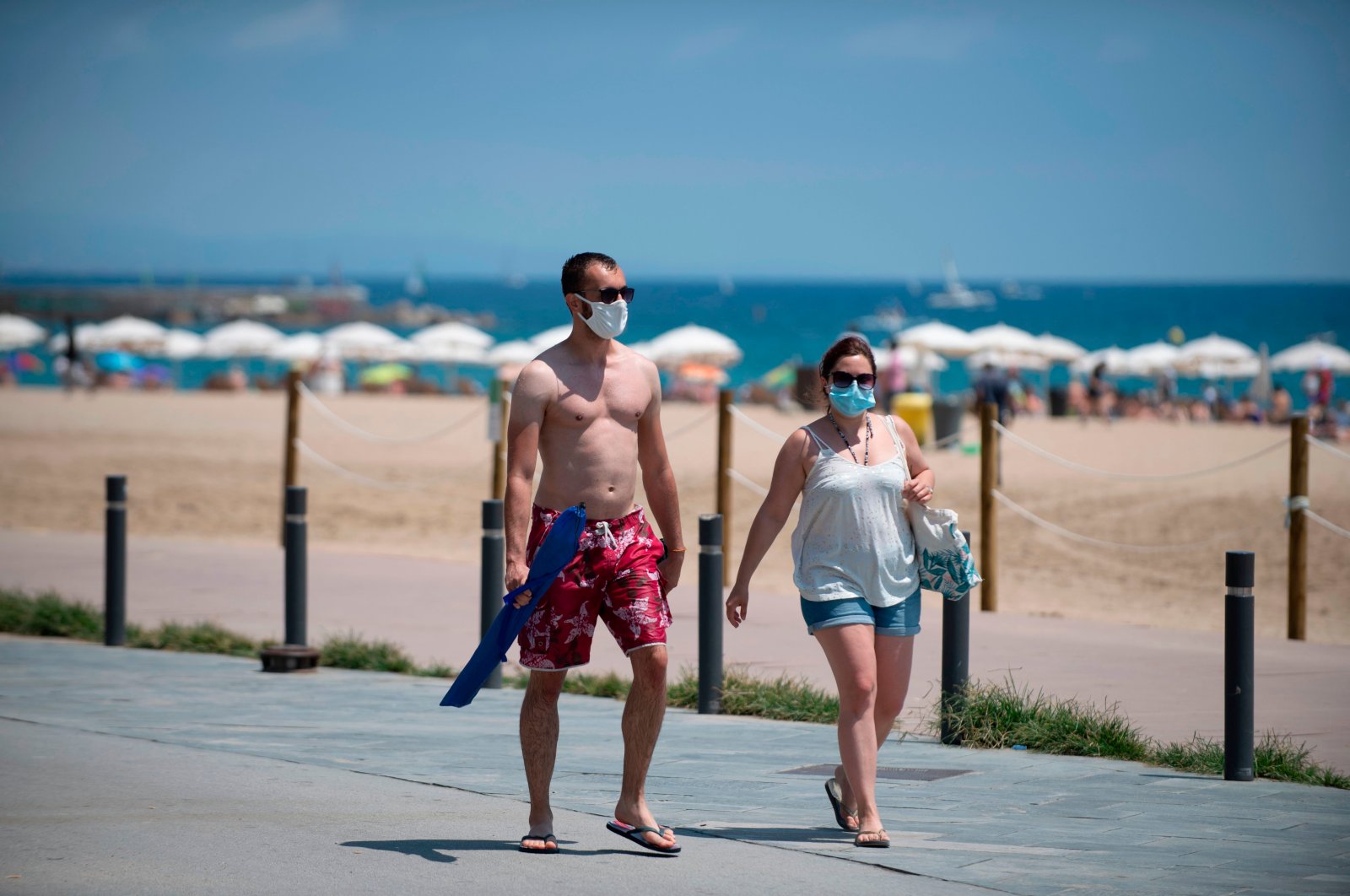 People wear face masks as they walk along a beach in Barcelona, July 18, 2020. (AFP Photo)