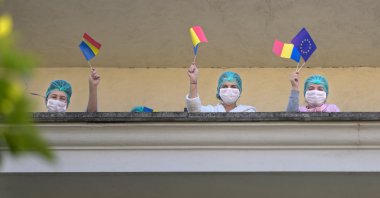 Medical staff of the Polizu maternity hospital hold European Union and Romanian flags while listening to a violinist playing to entertain them and the patients in Bucharest, Romania, Tuesday, April 28, 2020. (AP Photo)
